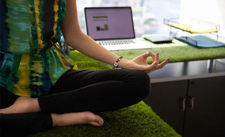 A person meditating at a modern office desk adorned with artificial grass, promoting a healthy, mindful workspace.