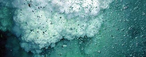 Turbulent underwater scene with a powerful white foam surge and countless bubbles in deep teal water, representing harsh conditions.