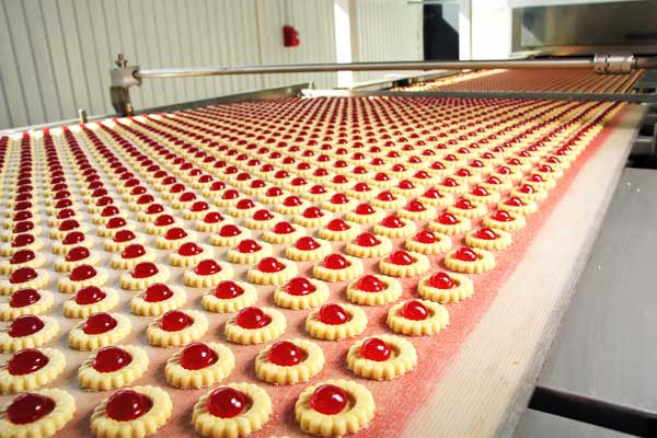 Endless rows of uniform cookies with shiny red jelly on a factory conveyor, where pH control ensures consistent quality.