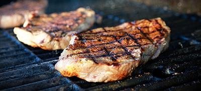 Steaks sizzling on a hot grill, ready for temperature checks to ensure food safety.