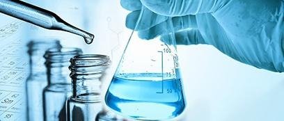 Gloved hand holds flask with blue liquid, dropper, and vials for scientific water quality analysis.
