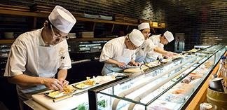 Dedicated sushi chefs meticulously prepare various fresh sushi pieces behind a sparkling counter.