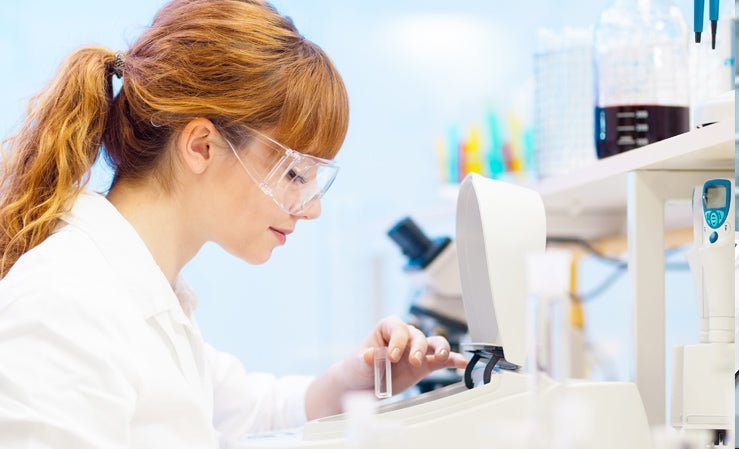A focused scientist in safety goggles loads a sample into a UV-Vis spectrophotometer in a lab.