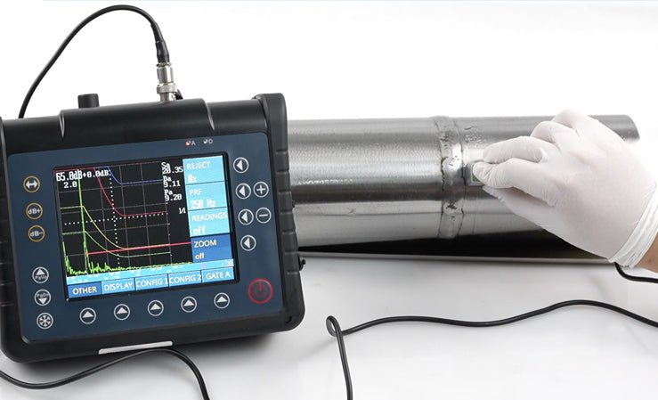A gloved hand performs ultrasonic non-destructive testing on a welded metal pipe using a portable NDT device.