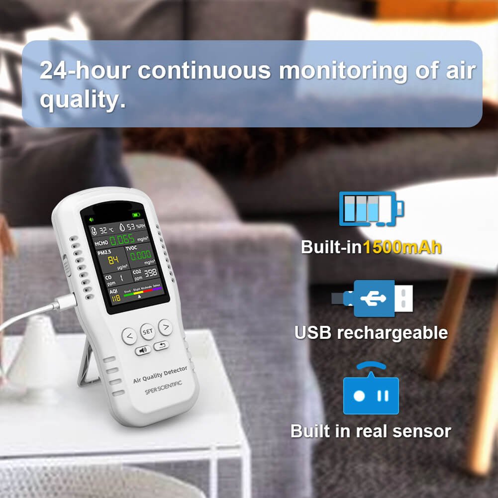 White handheld air quality monitor by Sper Scientific showing readings on its screen, displayed on a white table with a blurred background.