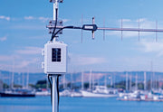 White wireless long-range repeater with solar power by Davis Instruments mounted on a silver pole against a blurred water and boat background.
